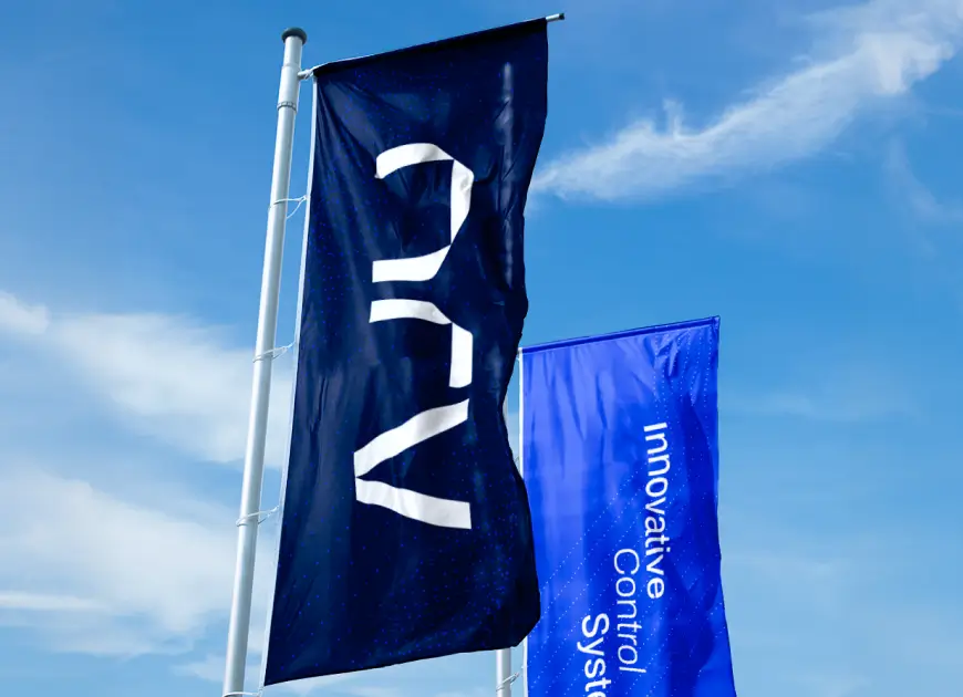 Two large corporate flags waving against a blue sky featuring the geometric dark blue monogram branding and modern typography developed for the Latin America market hub.