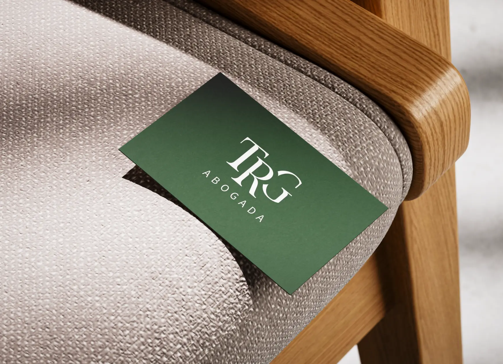 Premium green texture business card with white TRG Abogada logo placed elegantly on a modern wooden office chair.