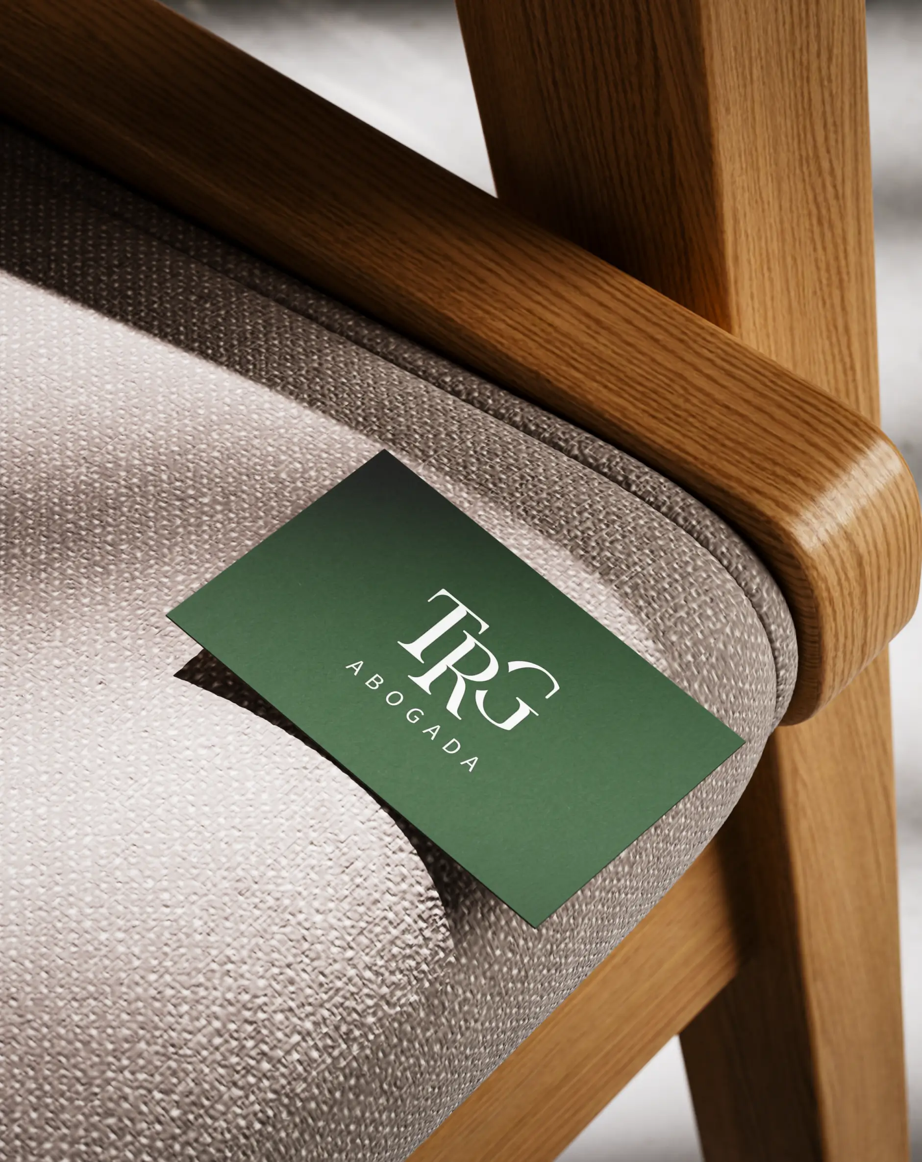 Minimalist green business card featuring the white TRG Abogada corporate monogram resting on a modern textured fabric chair.