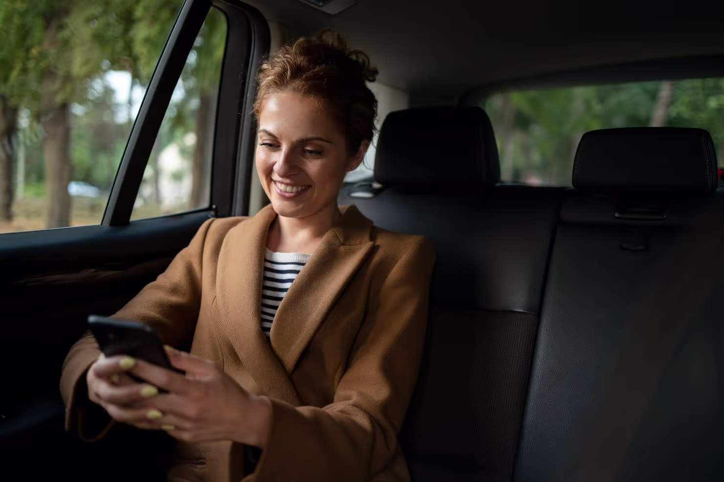 a lady using her phone in the backseat of a car and smiling.