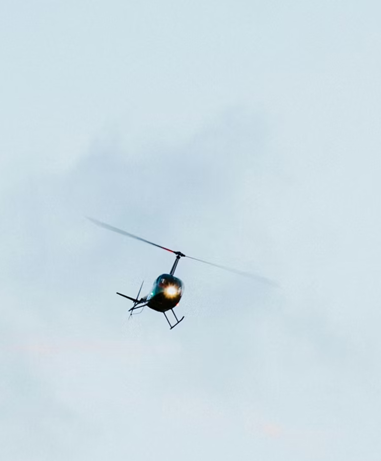 Helicopter with its light on flying against a pale blue sky.