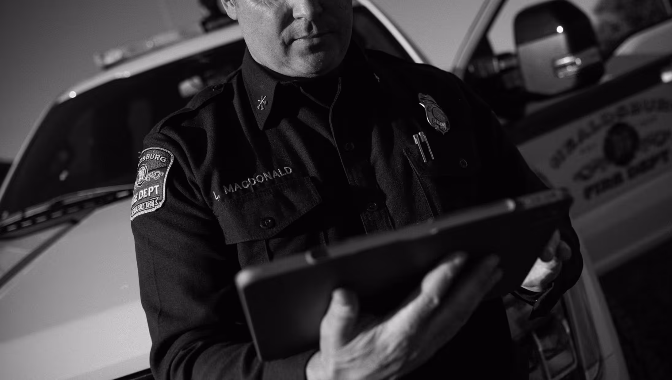 Firefighter in uniform holding a tablet device in front of a fire department vehicle.