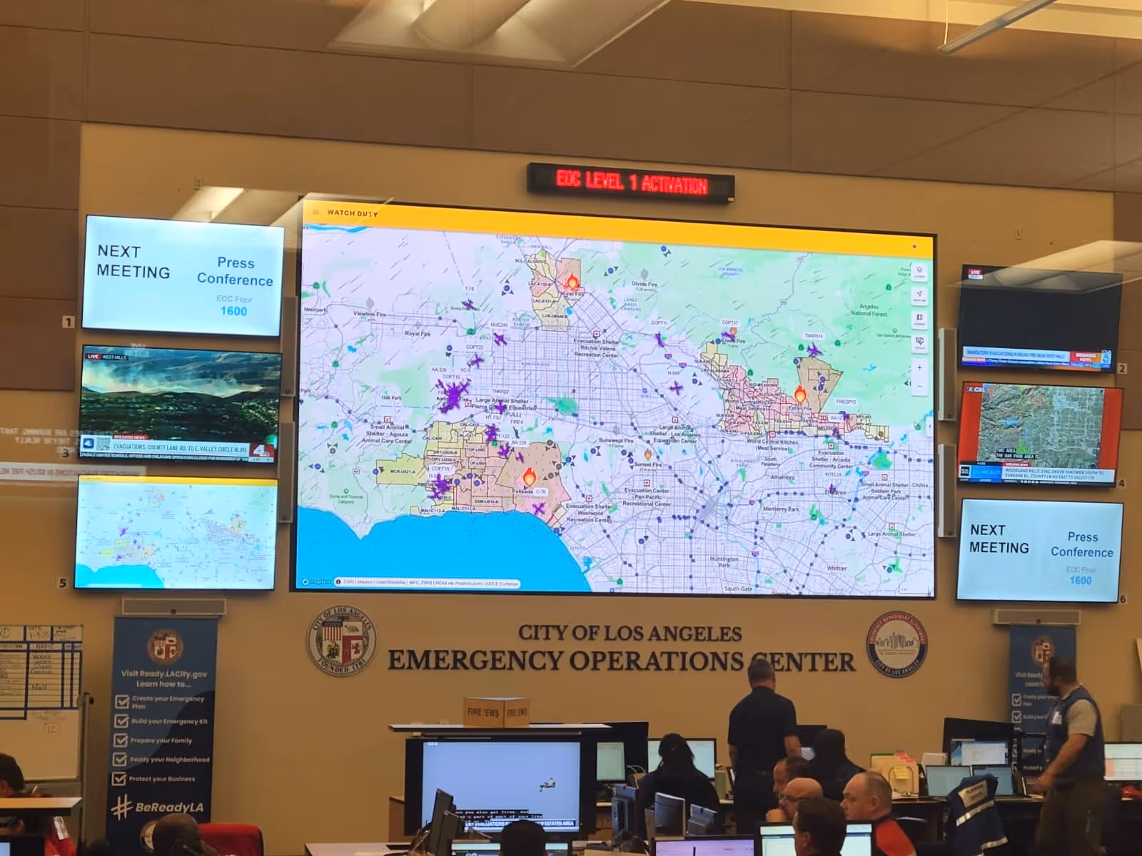 Emergency Operations Center in Los Angeles with multiple screens showing fire maps and evacuation information.
