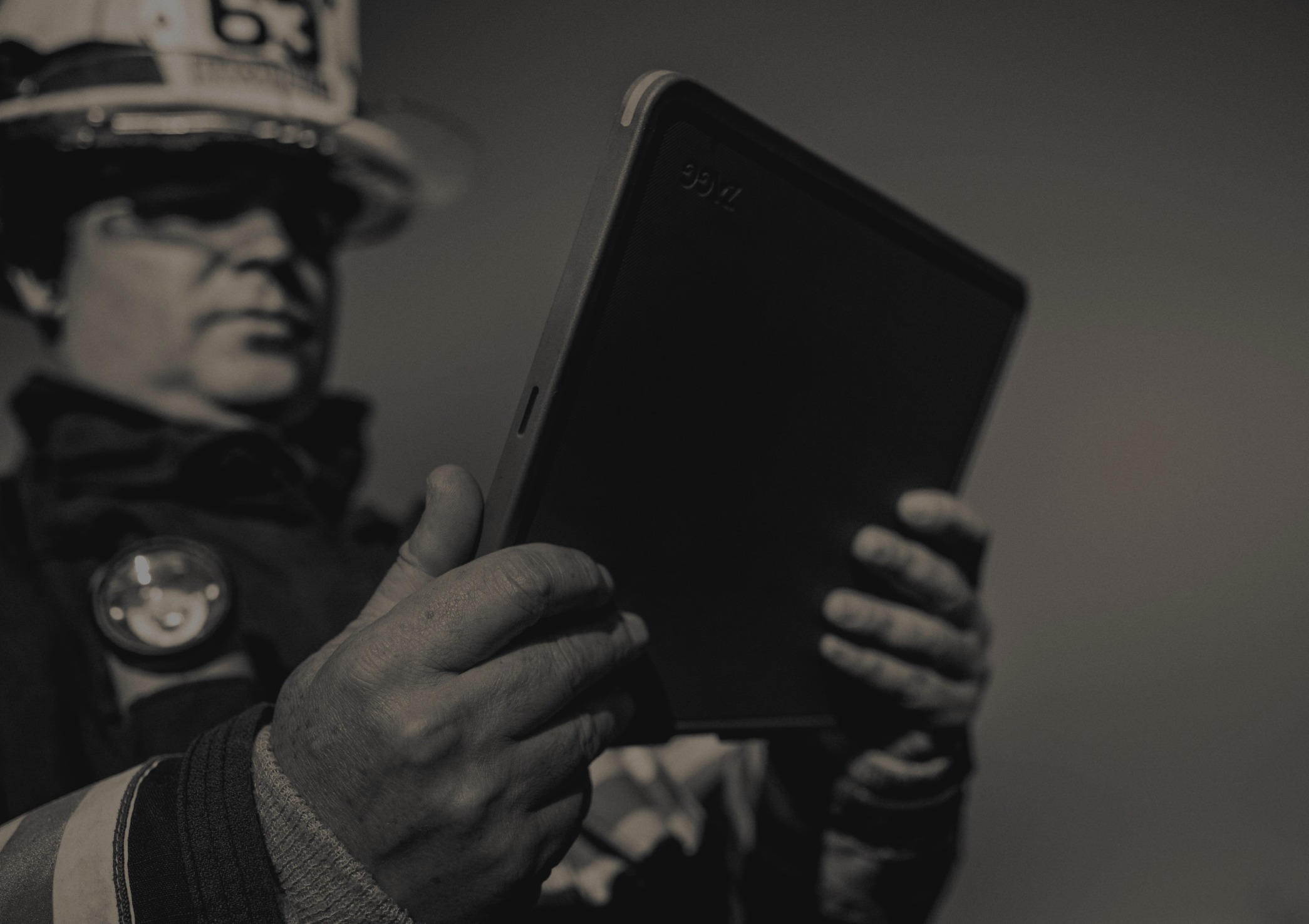 Firefighter in uniform holding and looking at a tablet device outdoors.