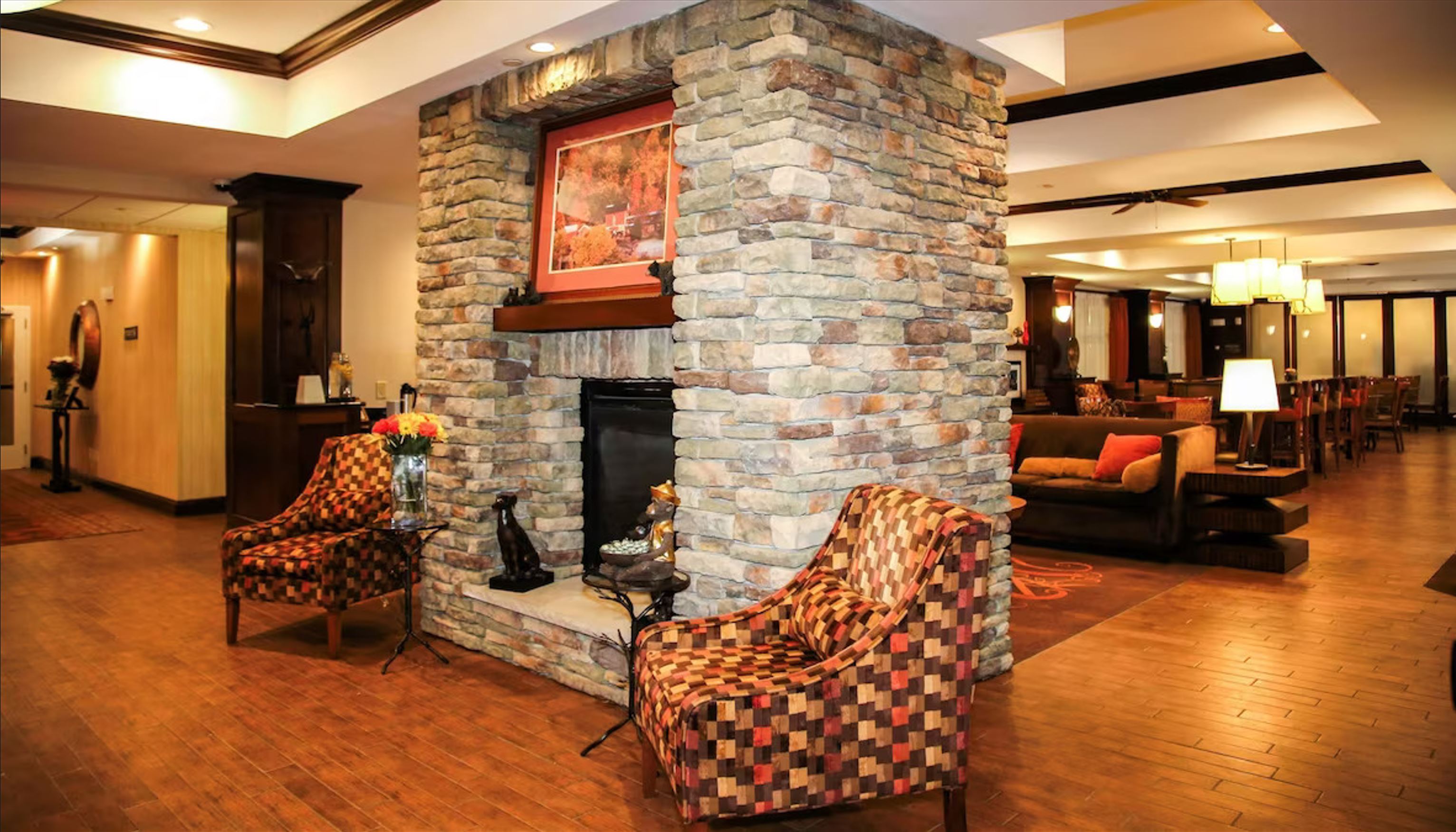 Outdoor patio area with stone-built barbecue grill, black chairs and tables, string lights, and multi-story beige residential buildings in the background.