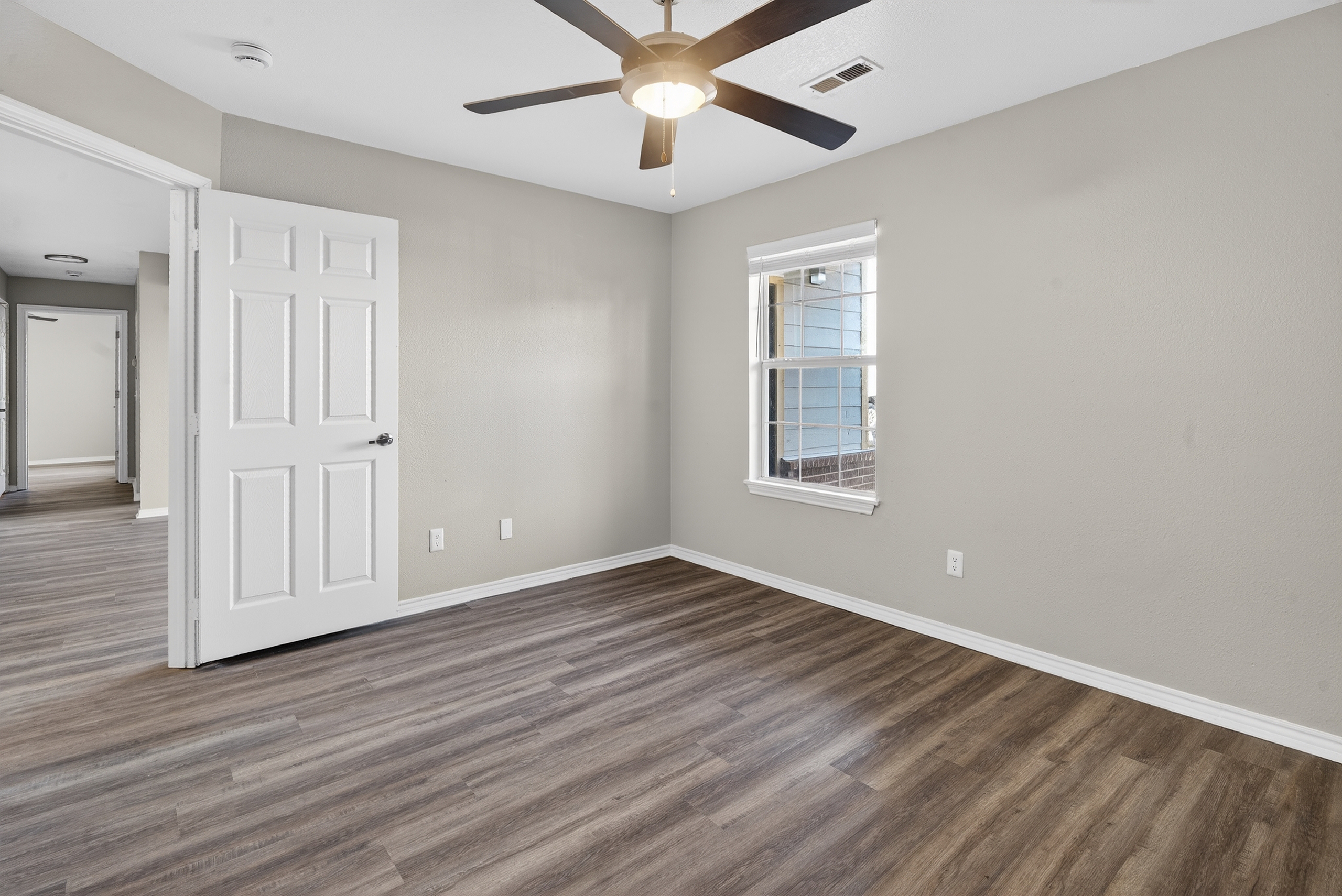 Unfurnished bedroom with ceiling fan, window and view down hallway