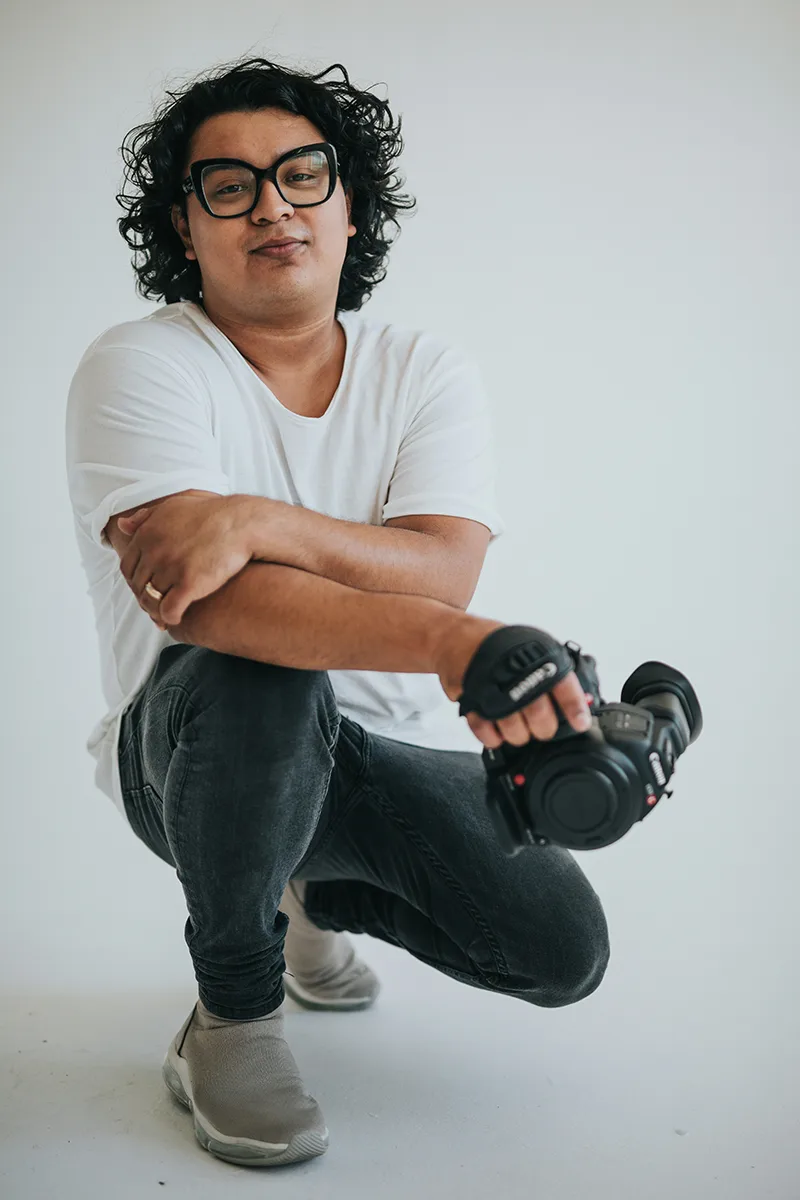 Portrait of a man sitting cross-legged holding a camera and smiling.