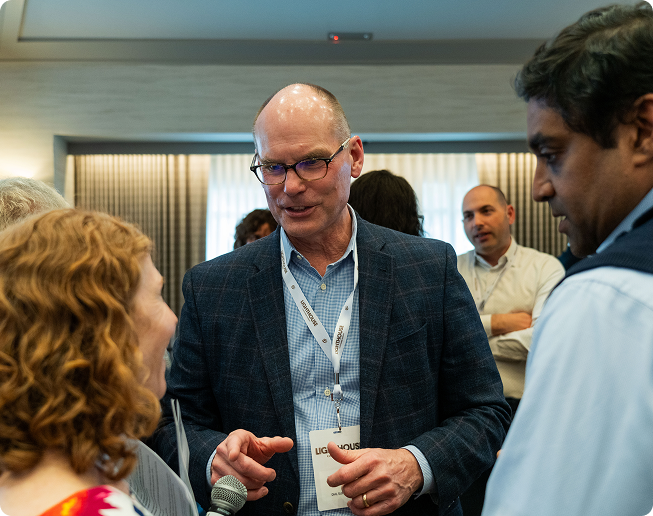 Man in glasses and a checked blazer speaking to a woman with curly red hair and a man with dark hair at a networking event.