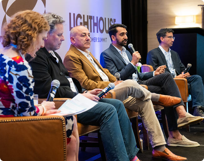 Five panelists seated on a stage during a discussion at the Lighthouse Customer Summit, with one man speaking into a microphone.