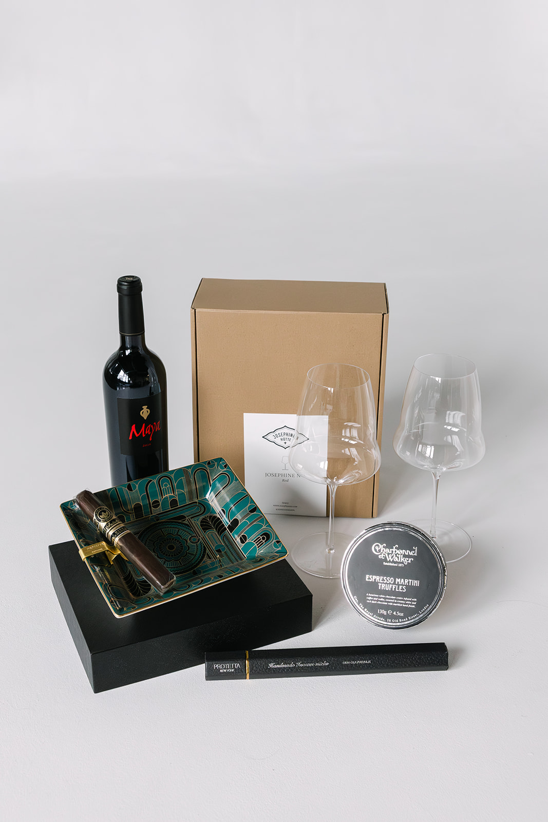 Gift set including a bottle of Maya wine, two clear wine glasses, a decorative ashtray with a cigar, a box of espresso martini truffles, and a box of handcrafted incense sticks.