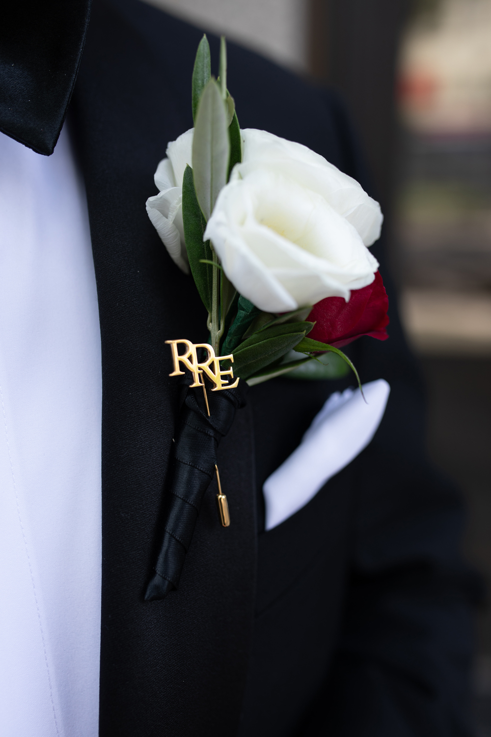 White and red boutonniere pinned to a black tuxedo jacket with a white shirt and pocket square.