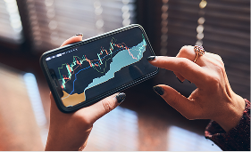 Person holding a smartphone displaying colorful financial stock market charts.