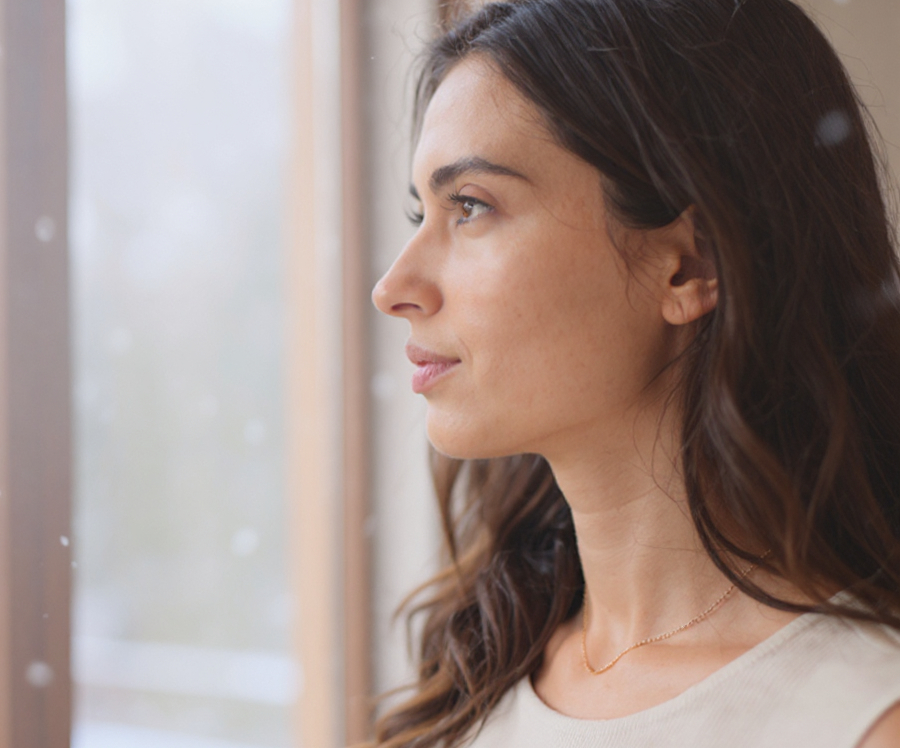 A woman staring out of a window, reflecting on the differences between PMDD vs bipolar.