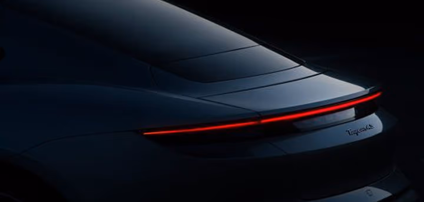 Rear view of a sleek dark car with illuminated thin red taillight strip in a dimly lit setting.