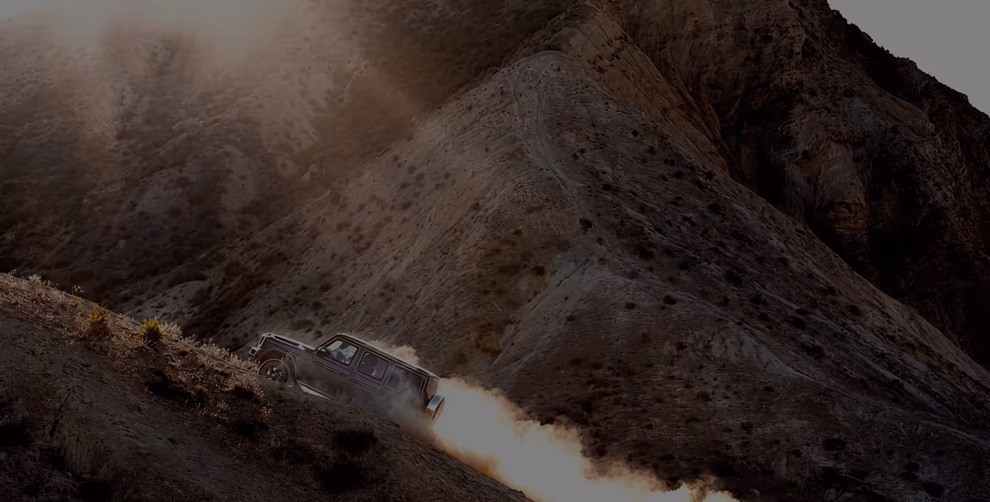 SUV driving uphill on a dusty, steep mountain trail with rugged terrain.