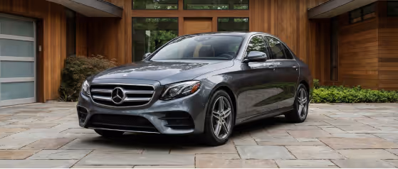 Gray Mercedes-Benz sedan parked on a stone driveway in front of a modern wooden house.