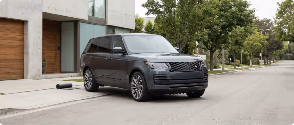 Black luxury SUV parked on a quiet residential street near modern houses and trees.