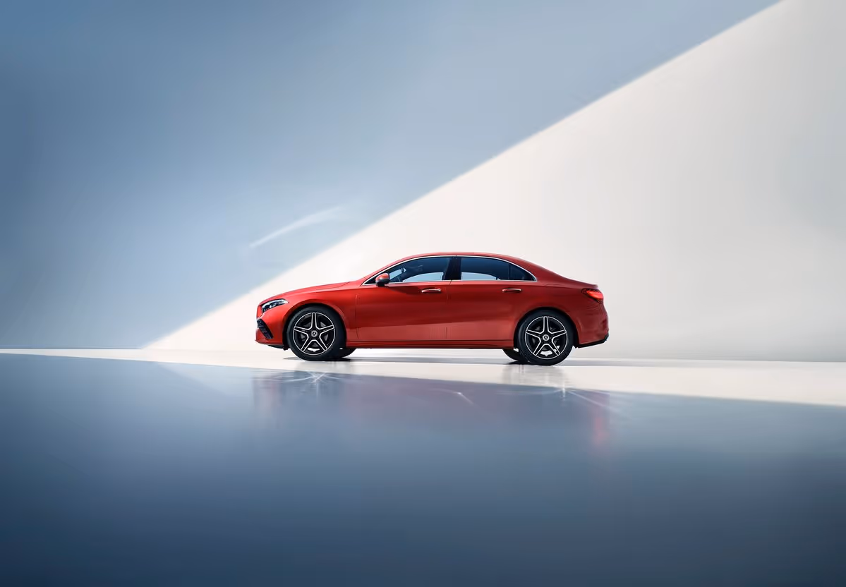 Side view of a red luxury sedan parked indoors with soft natural light and smooth reflections on the floor.
