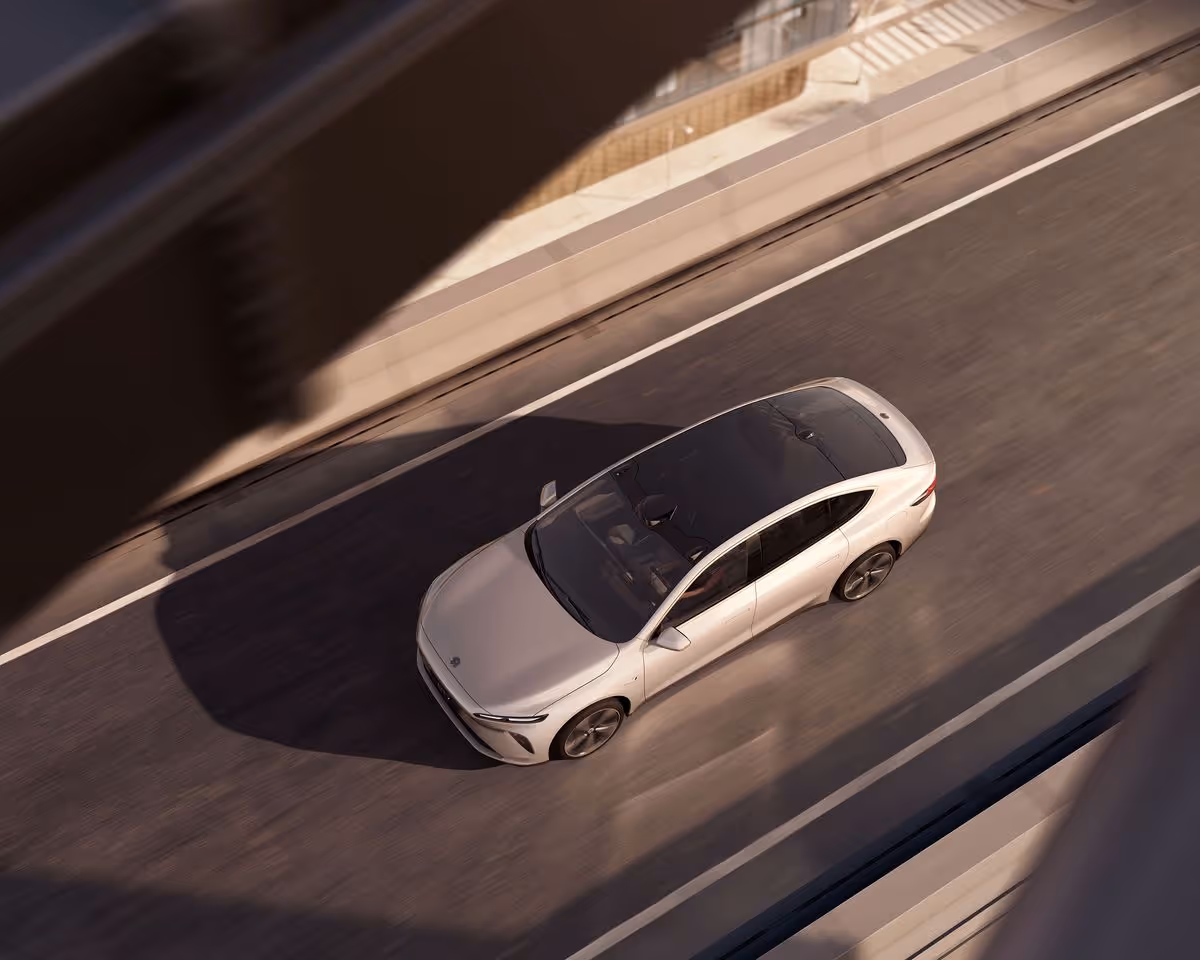 White electric car with black roof driving on a highway seen from above with shadows crossing the road.