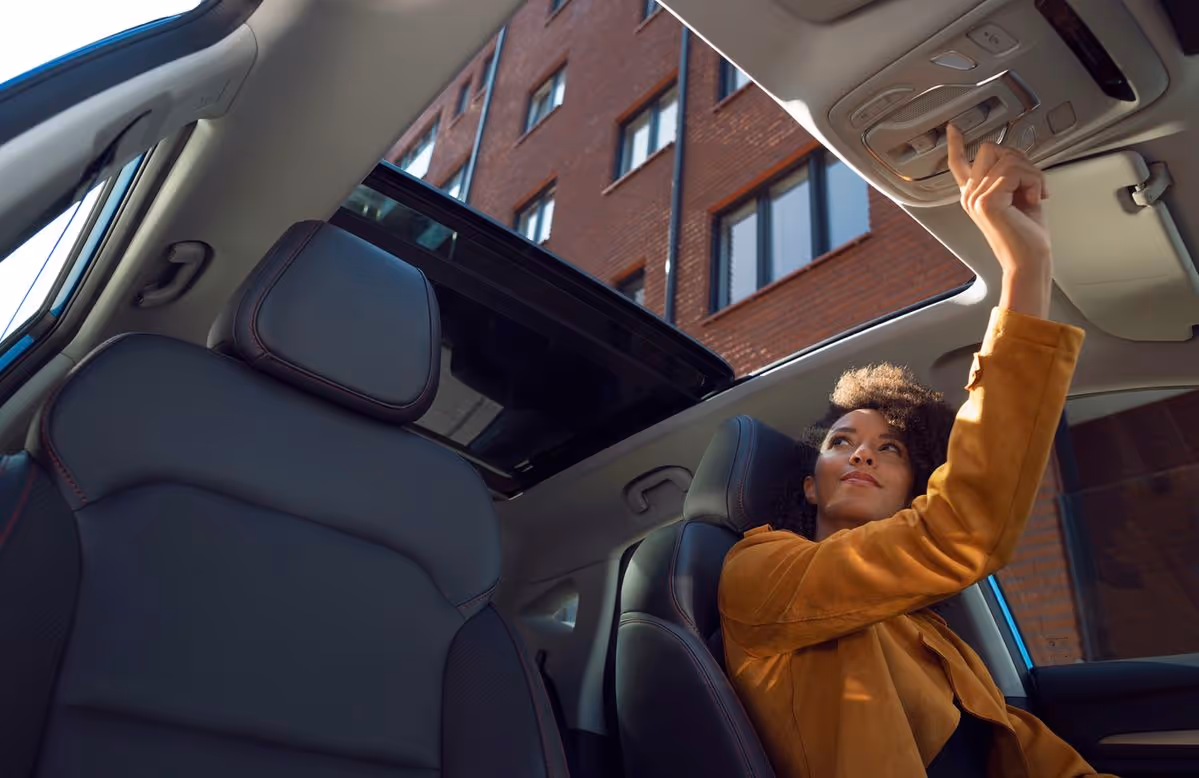 Person inside a car reaching up to press a button on the overhead console near an open sunroof.