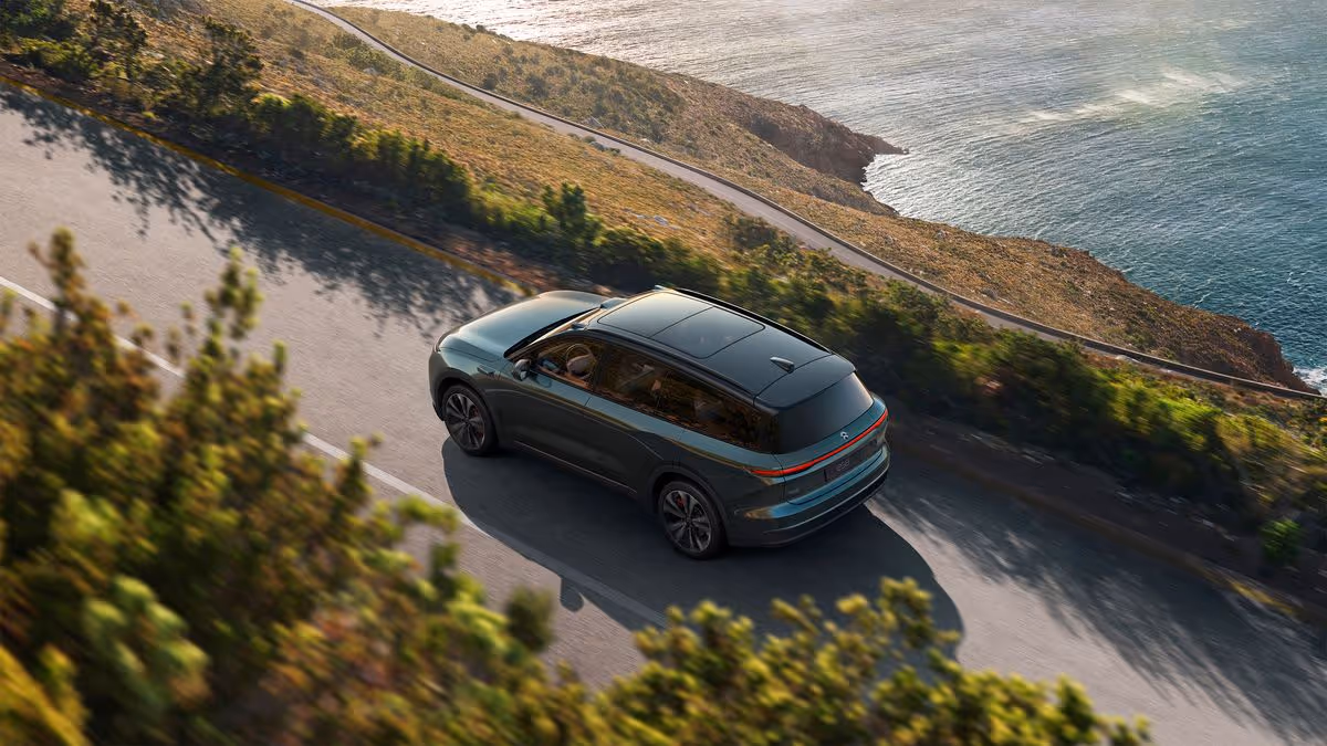 Dark green SUV driving on a coastal road with cliffs and ocean in the background.
