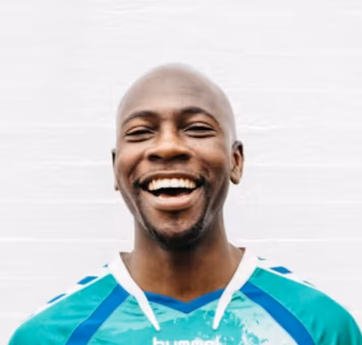 Smiling bald man wearing a turquoise and blue sports jersey against a light background.