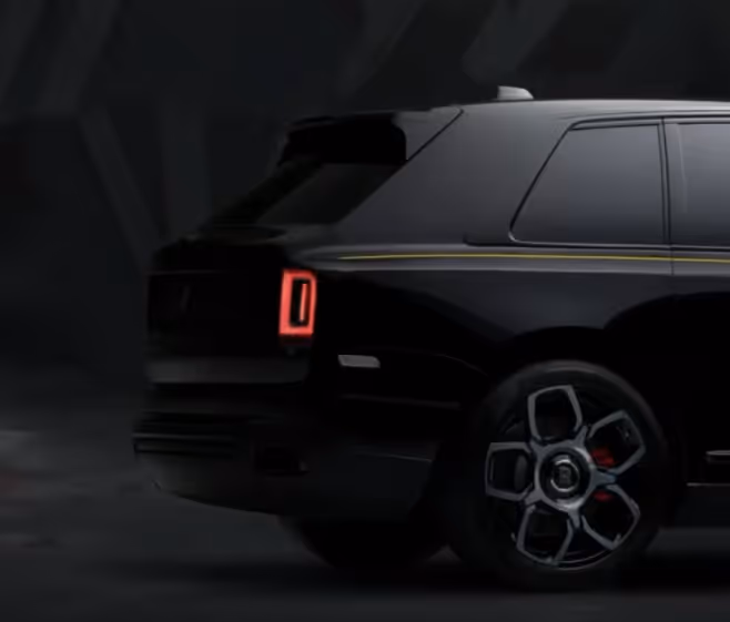 Rear side view of a black luxury SUV with illuminated red taillight and stylized alloy wheel in a dark setting.