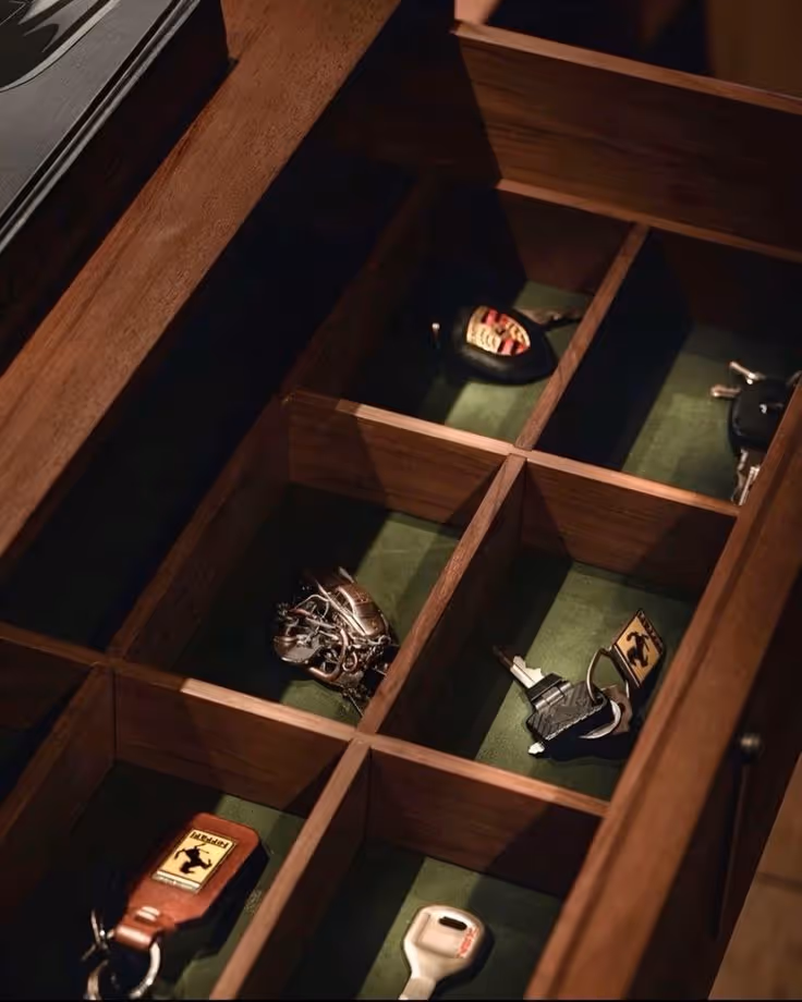 Open wooden drawer with nine compartments holding various car keys and keychains.