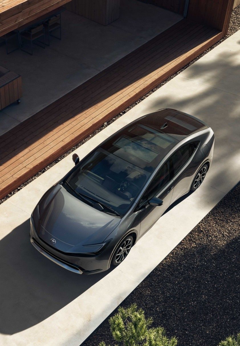 Overhead view of a sleek black electric car parked on a concrete driveway beside a modern wooden deck.
