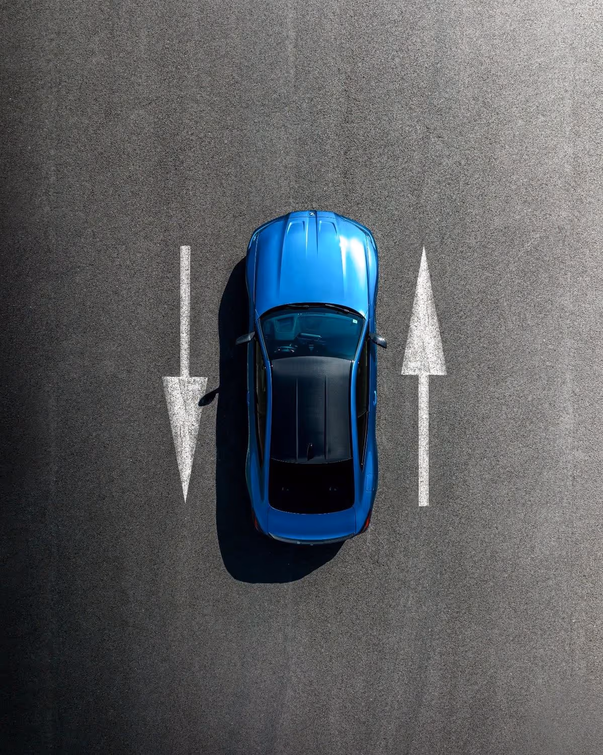 Top-down view of a blue car parked between two painted arrows on asphalt, one pointing left and one pointing right.