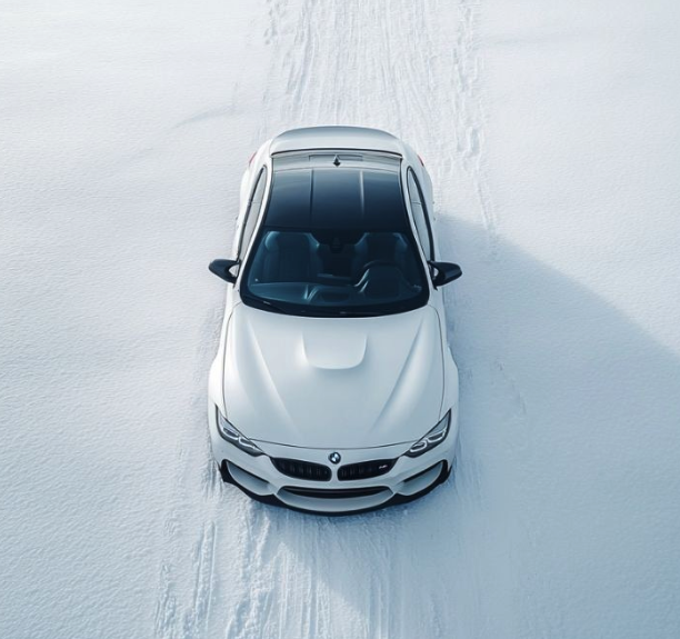 White BMW car driving through snow, viewed from above showing tire tracks.