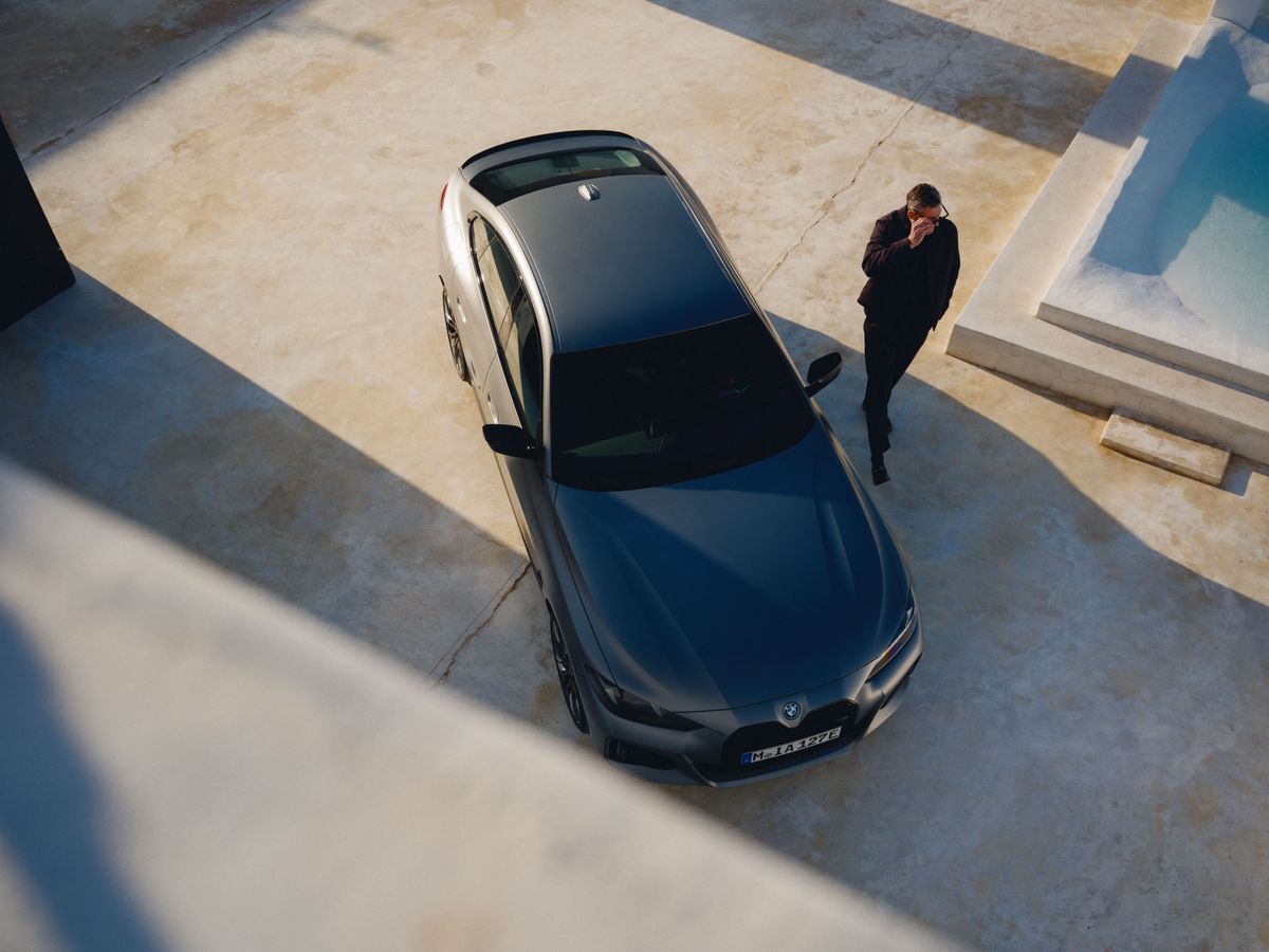 Overhead view of a silver BMW parked on a concrete surface with a man in dark clothes walking beside it near a light blue pool.
