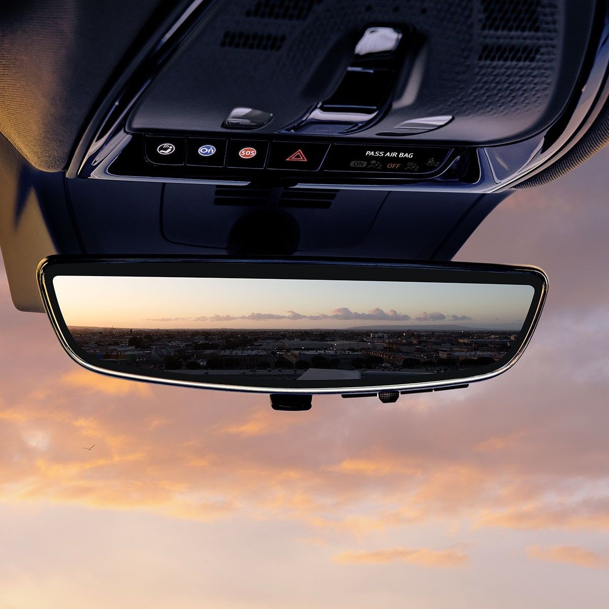 Rearview mirror reflecting a cityscape at sunset with orange clouds in the sky.
