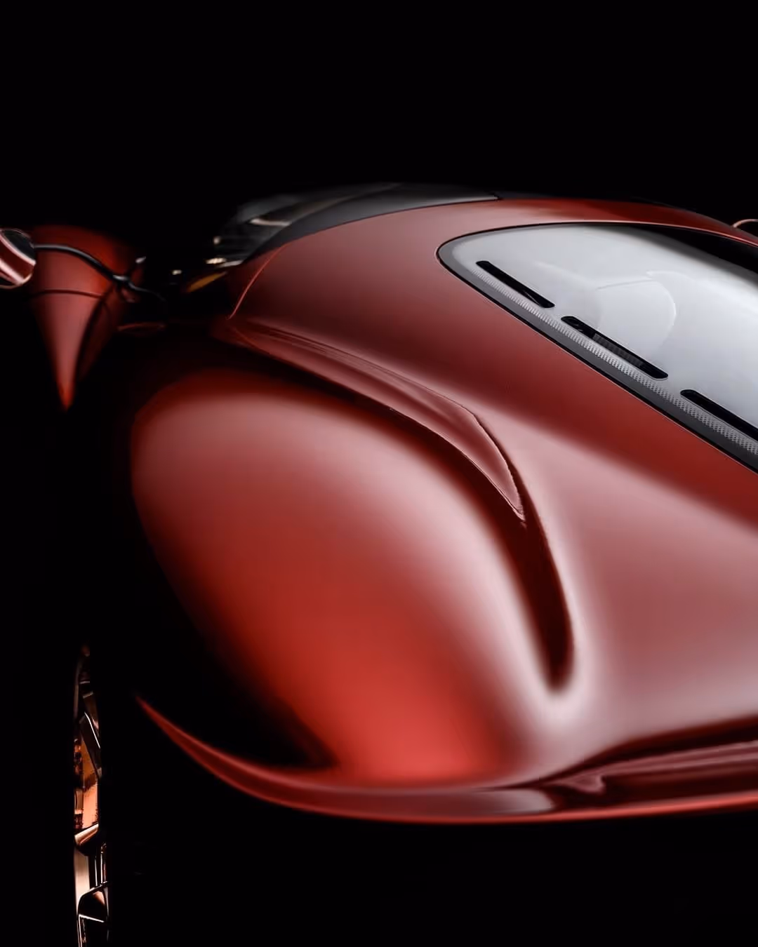 Close-up of a sleek, shiny red sports car hood with aerodynamic vents and a curved windshield against a black background.