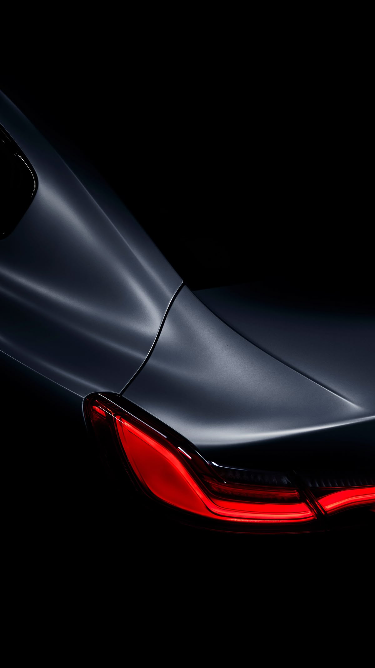 Close-up of a sleek car's rear with illuminated red tail light against a dark background.
