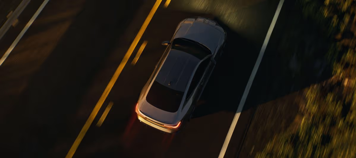 A silver car driving on a two-lane road at night with illuminated taillights and road markings visible.