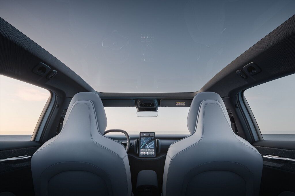 Interior view of a modern car showing gray front seats, a central touchscreen, steering wheel, and a large panoramic glass roof.