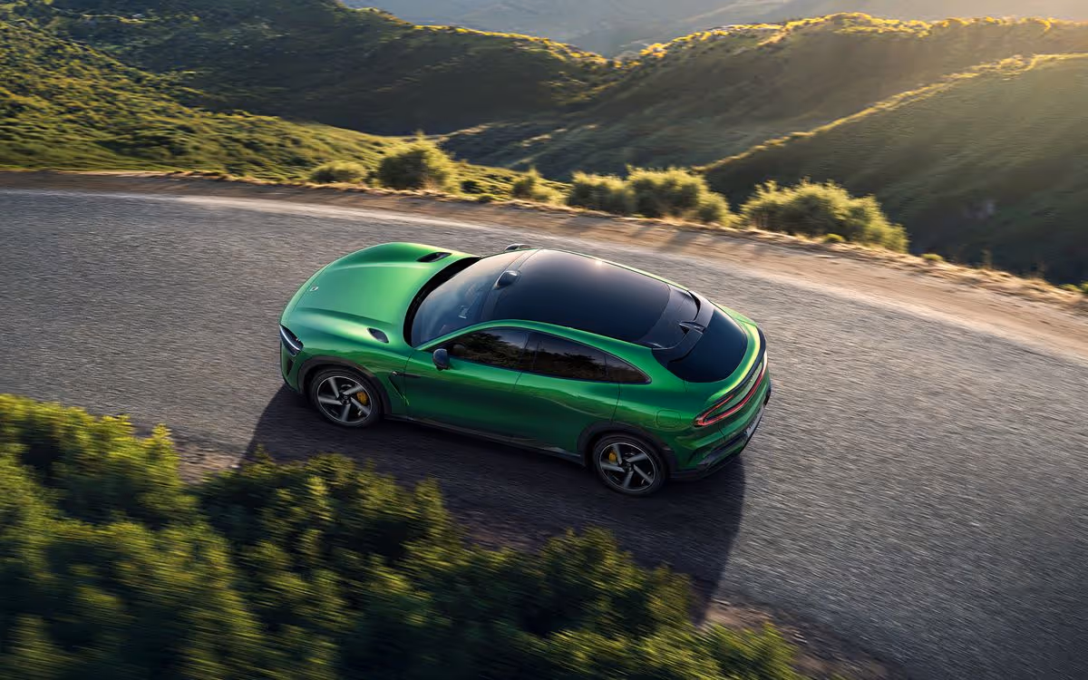 Green sports SUV driving on a winding mountain road with green hills and sunlight in the background.