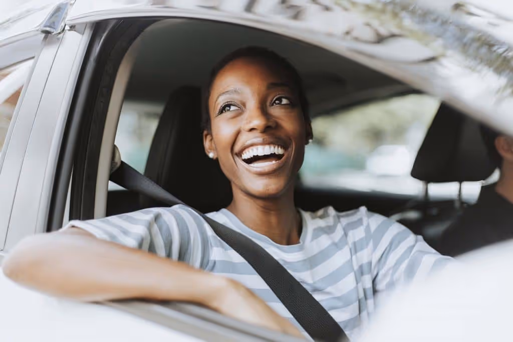 Smiling woman wearing a striped shirt sitting in a car with seatbelt fastened.
