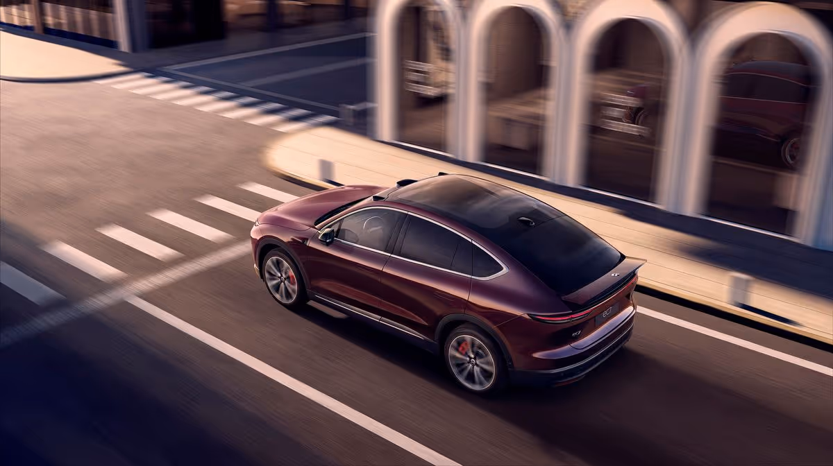 Maroon electric SUV driving on a city street near a building with arched windows.