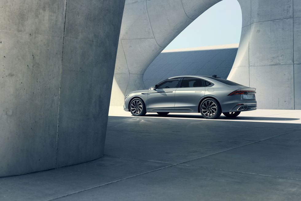 Silver modern sedan parked under large curved concrete architectural structures in daylight.