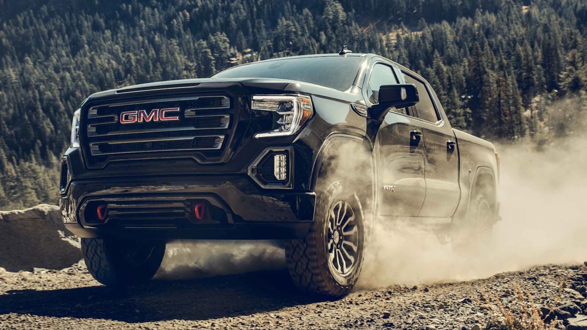 Black GMC pickup truck driving on a dusty off-road trail with forest in the background.