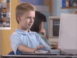Boy in a light blue shirt repeatedly clicking a computer mouse in front of an old desktop monitor.