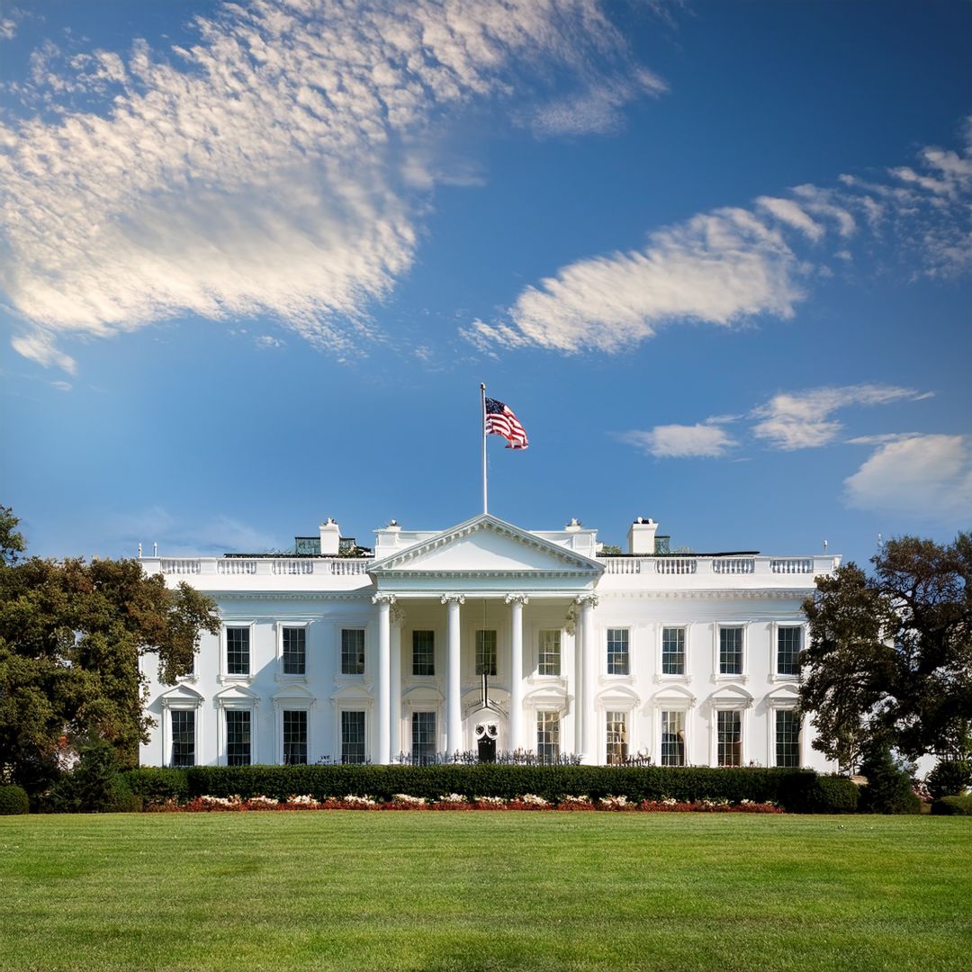 The White House with an American flag flying on top, under a blue sky with scattered clouds.