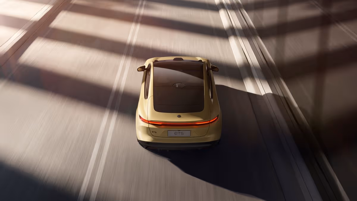 Top-down view of a beige electric sedan driving on a sunlit road with shadow patterns.