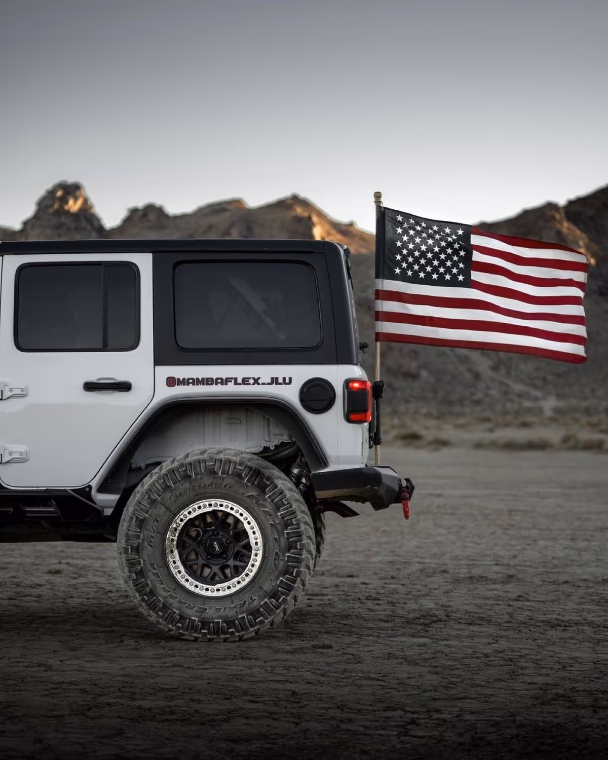 Rear side of a white off-road vehicle with an American flag mounted in a desert landscape.