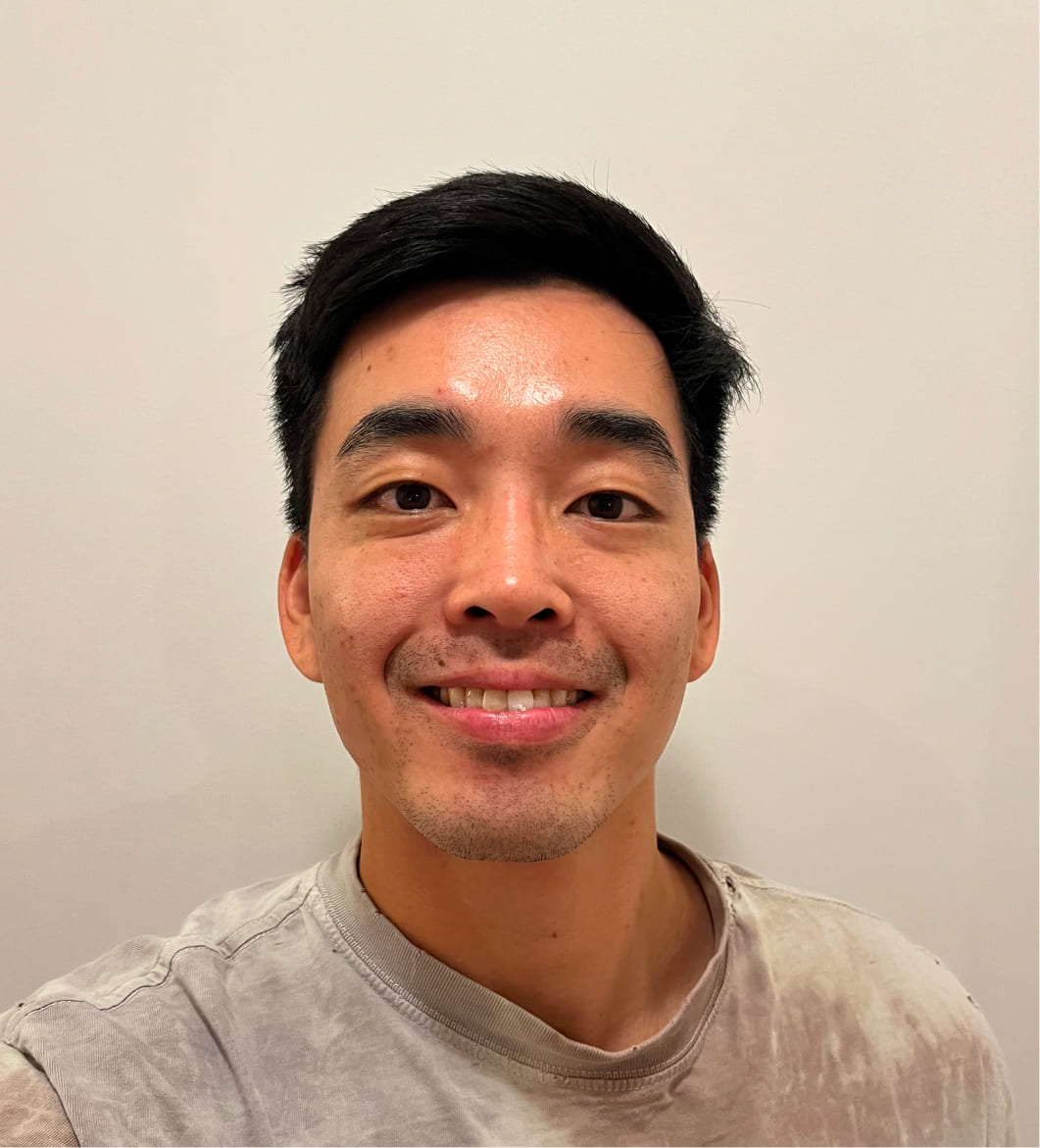 Smiling young Asian man with short black hair wearing a light-colored shirt against a plain background.
