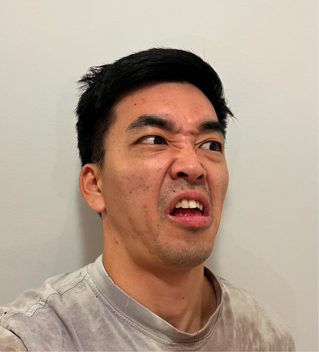 Man making a disgusted facial expression looking to the side against a plain light-colored wall.