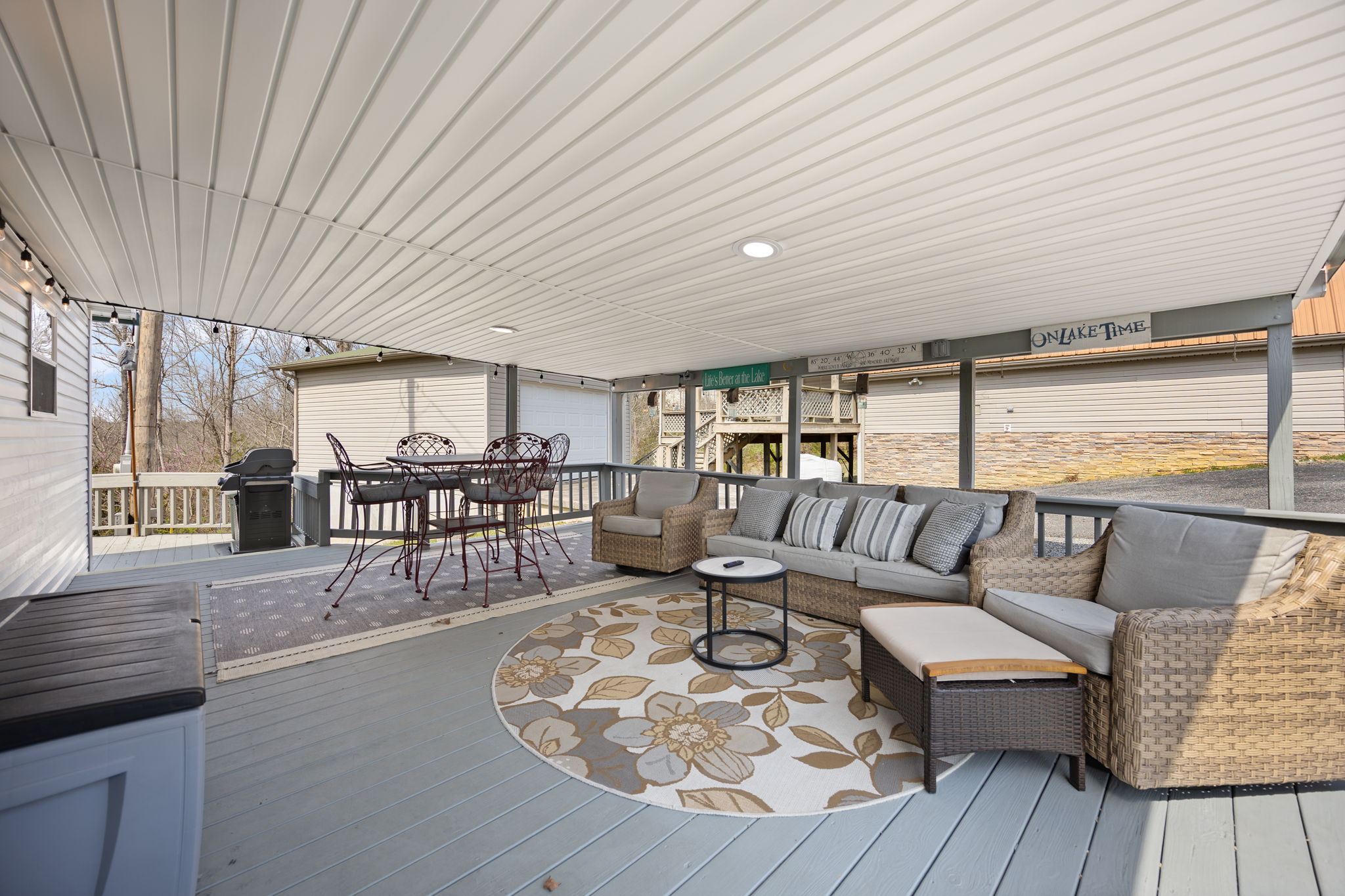 A-frame cabin with large glass windows and a brown roof next to a beige metal two-car garage on a grassy lawn with a gravel driveway.