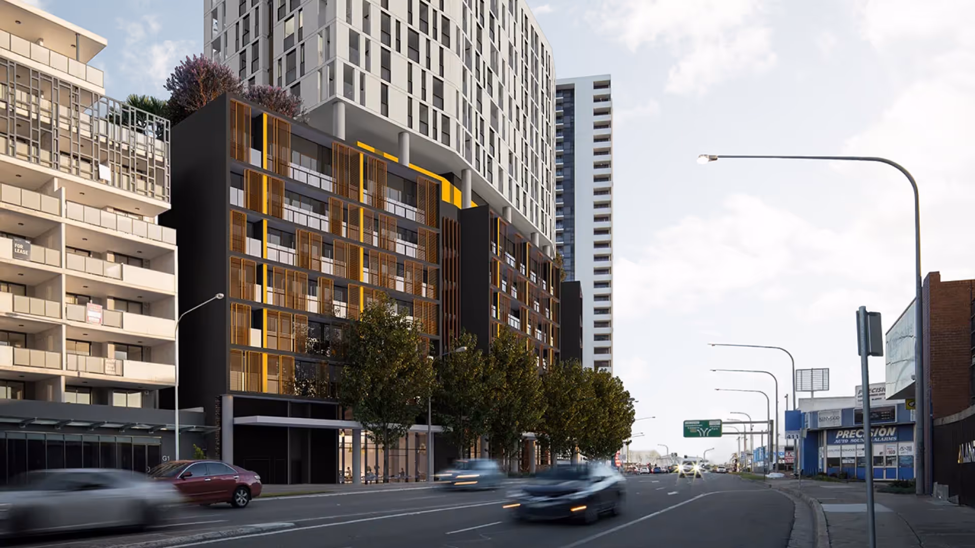 Urban street with modern multi-story buildings, trees along sidewalks, and cars driving by.